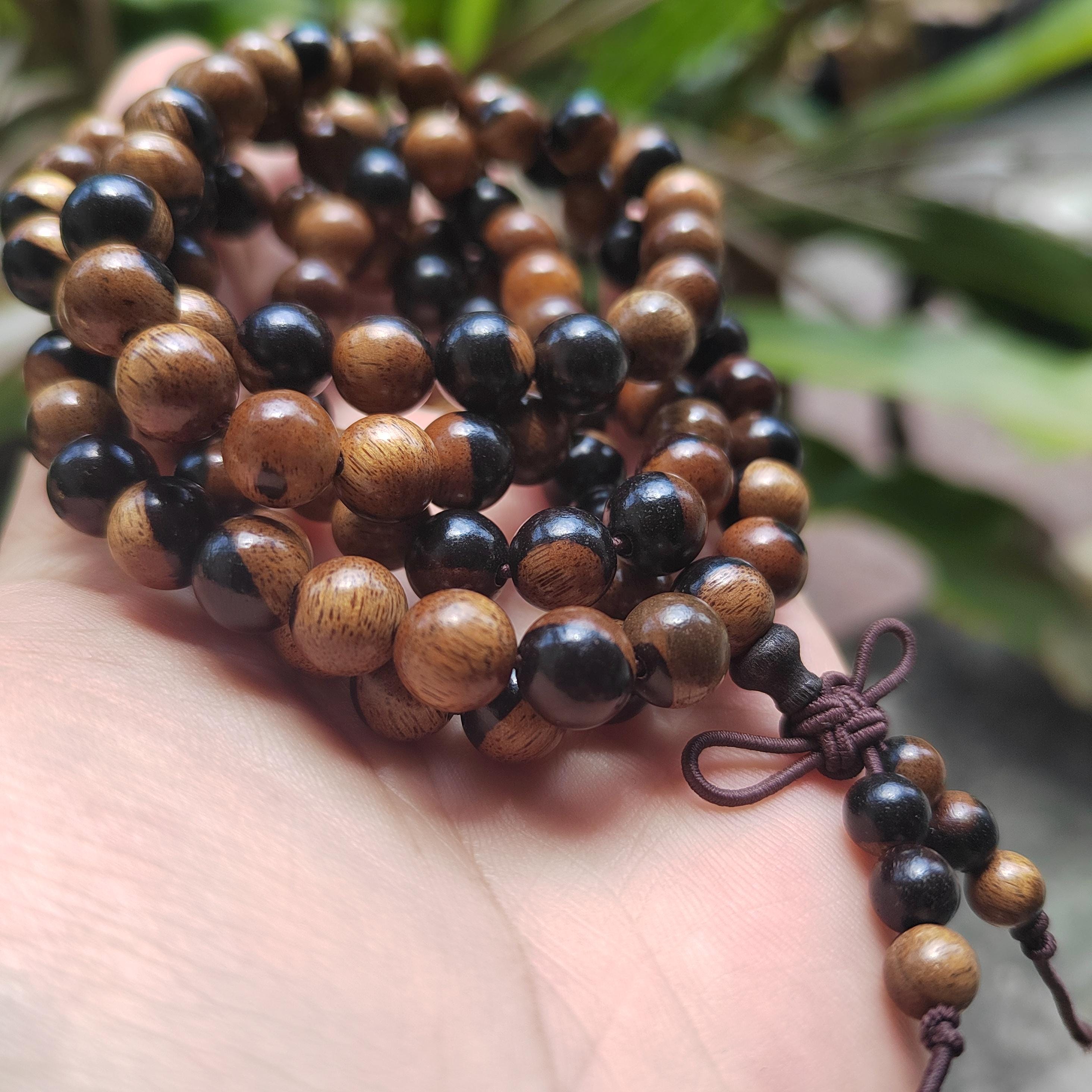 Wooden beaded bracelet with black and brown beads on a hand, blurred green leaves in the background