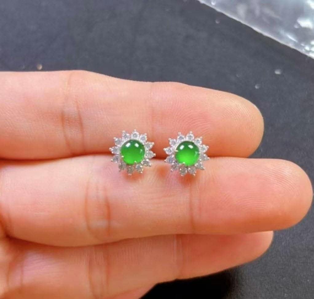 Green gemstone earrings held between fingers against a dark background