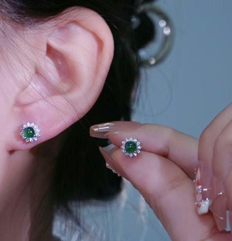 Close-up of a person wearing green gemstone earrings with a hand holding one earring.