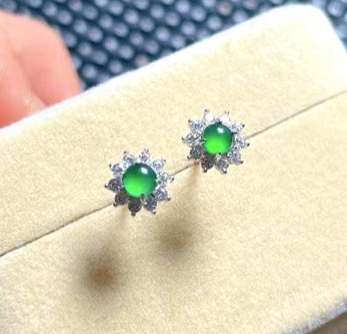 Green gemstone earrings on a white card with a blurred background