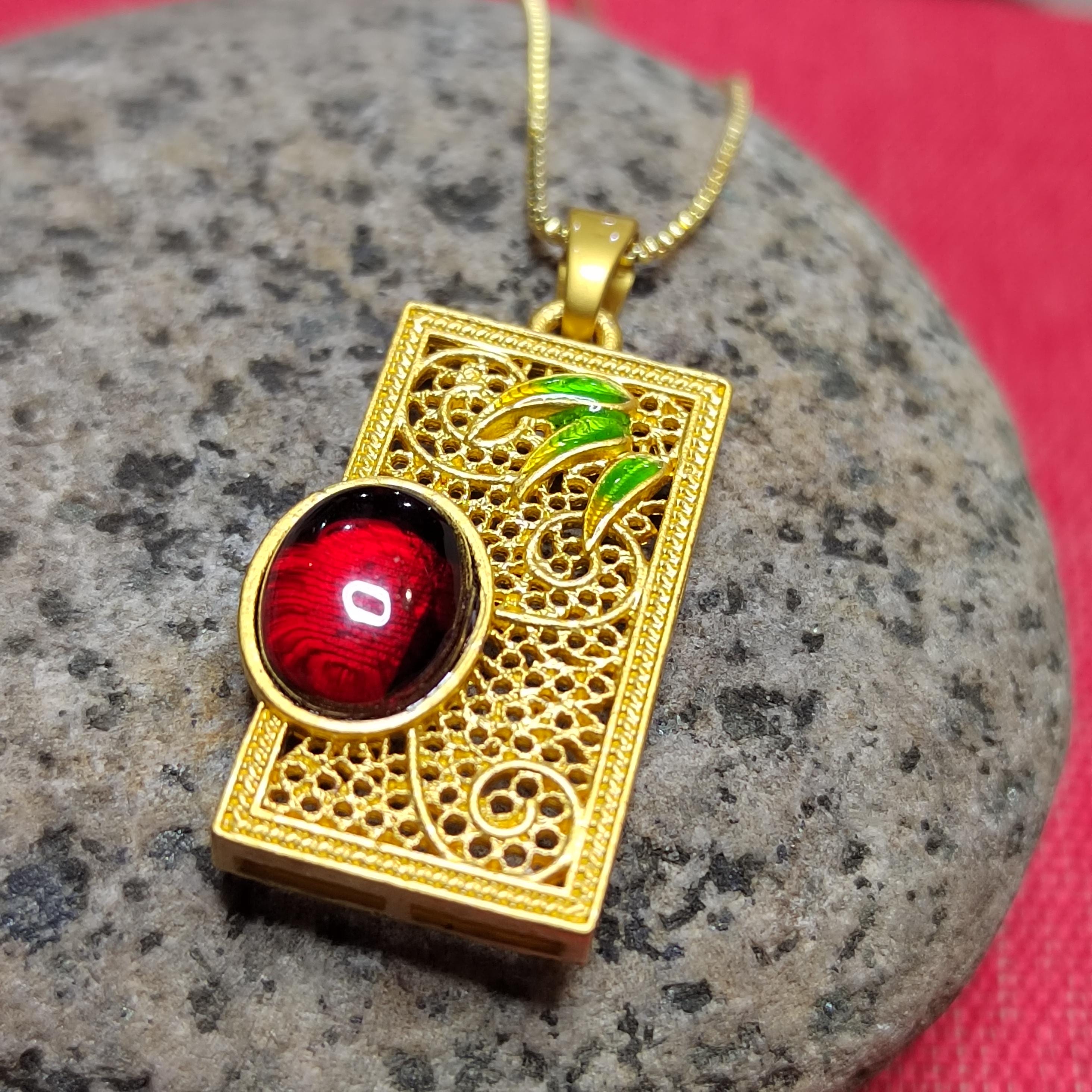 Gold pendant with amber and green leaves on a stone surface