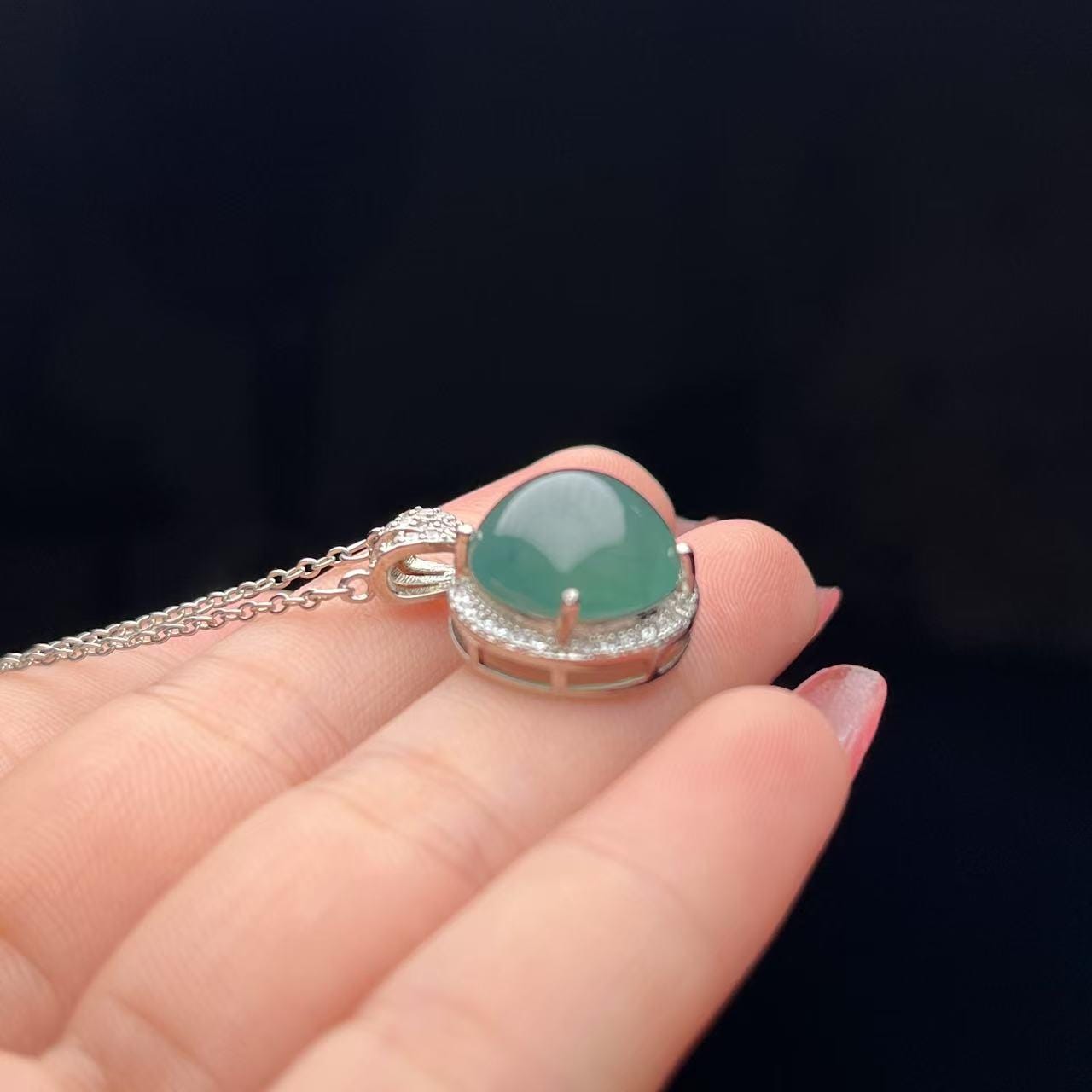 Green jade pendant on a chain held by a hand against a dark background