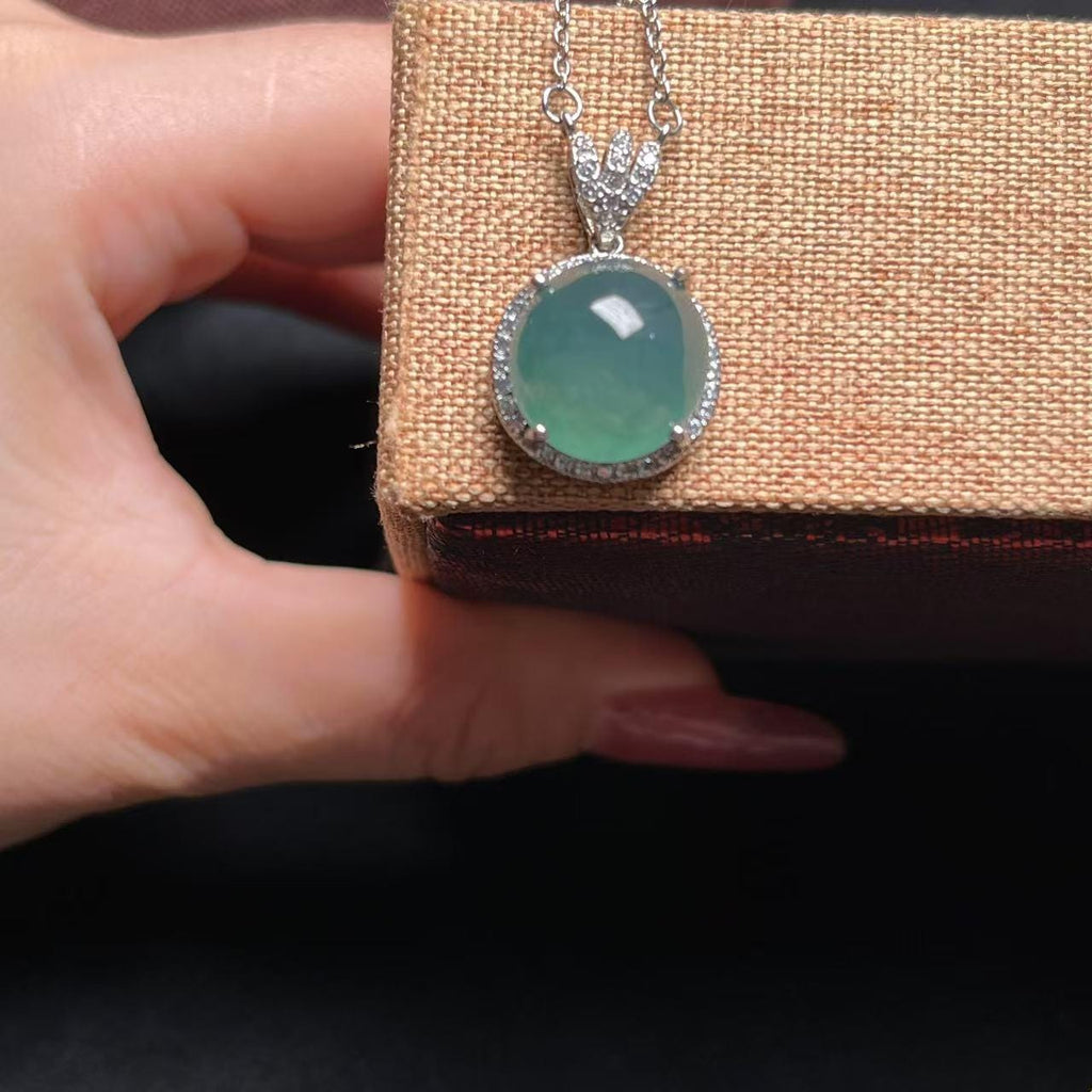 Green gemstone pendant on a chain held by a hand against a textured brown background