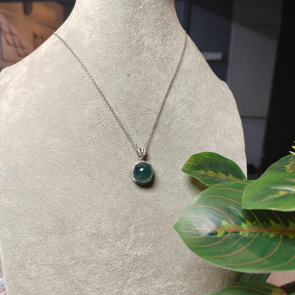Necklace with a green pendant on a mannequin bust, with a plant in the foreground.