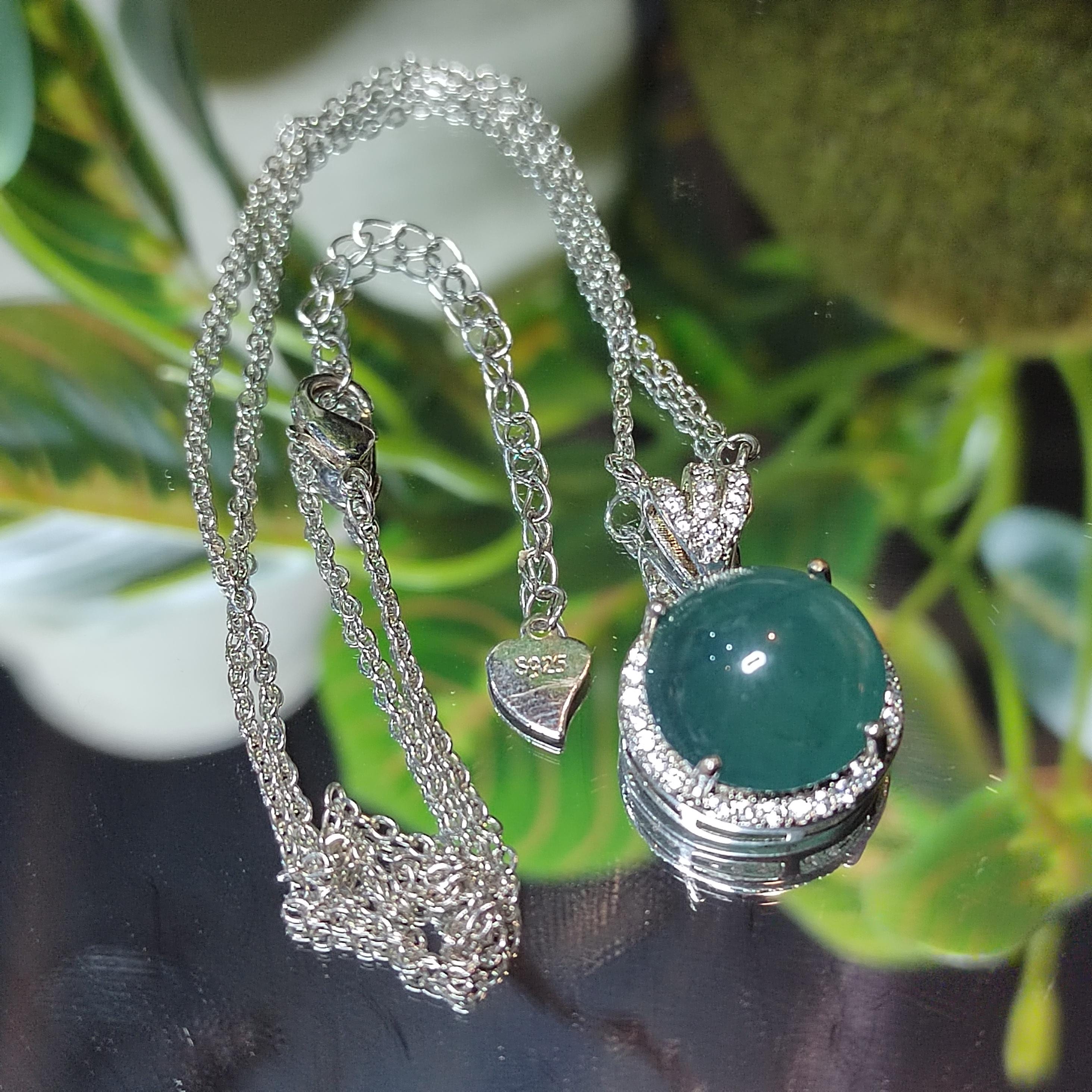 Silver necklace with a green gemstone pendant against a blurred green plant background