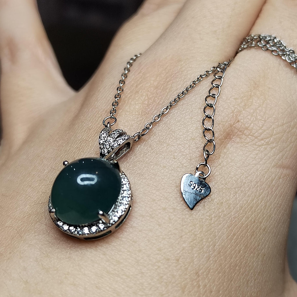 Necklace with a green pendant and heart-shaped charm on a person's wrist.