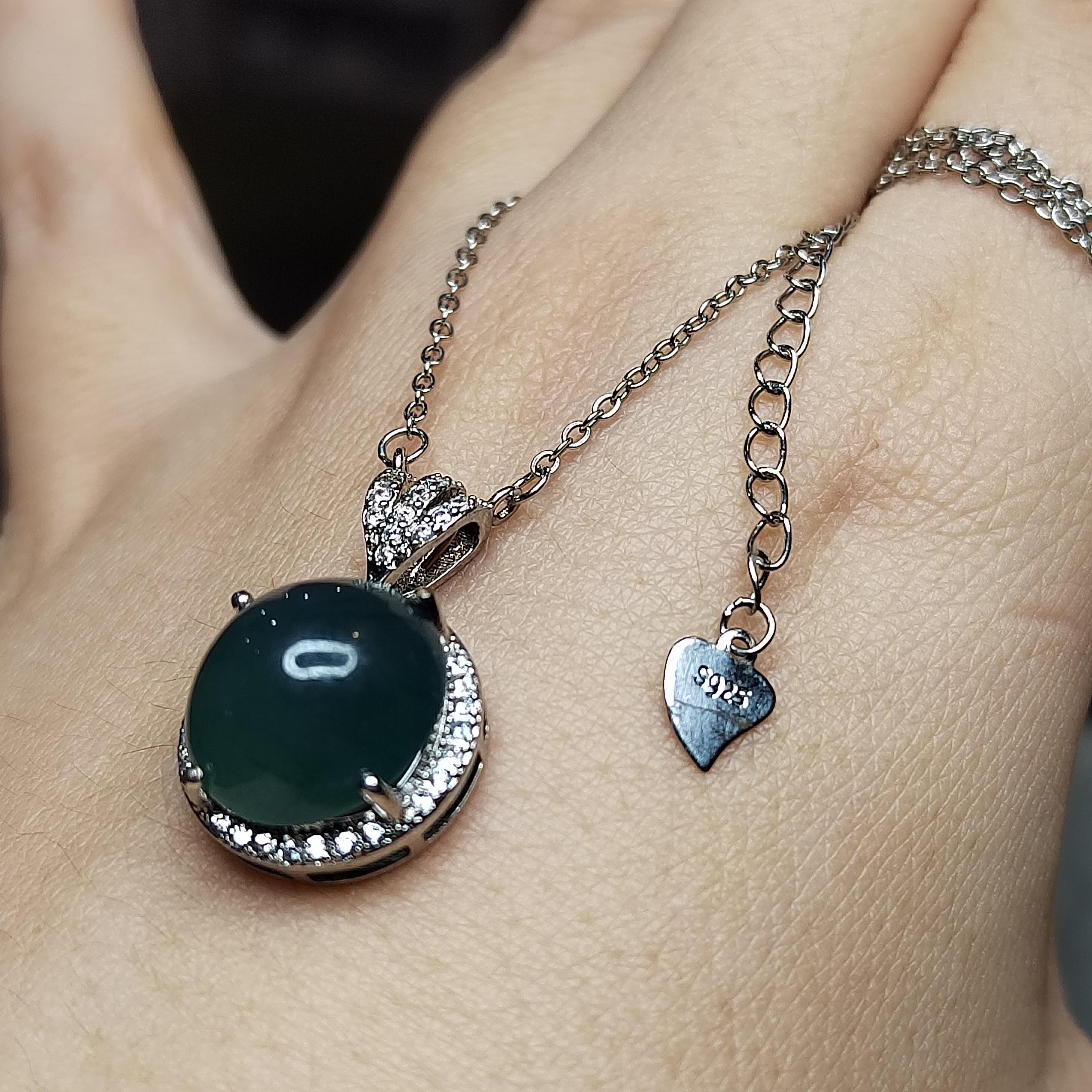 Necklace with a green pendant and heart-shaped charm on a person's wrist.