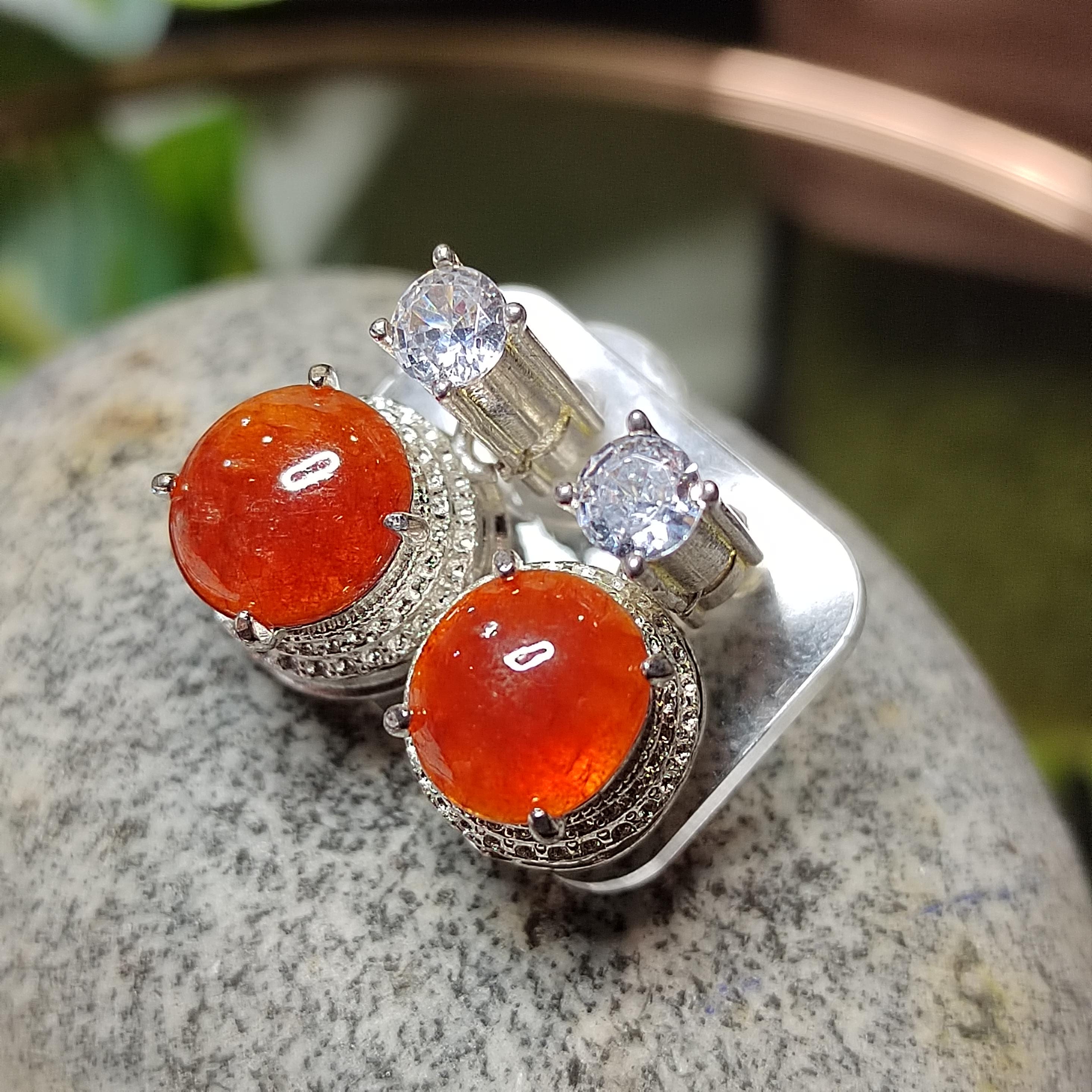 Silver earrings with orange gemstones on a stone surface