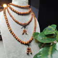 Wooden beaded necklace and earrings on a mannequin bust with green leaves in the background