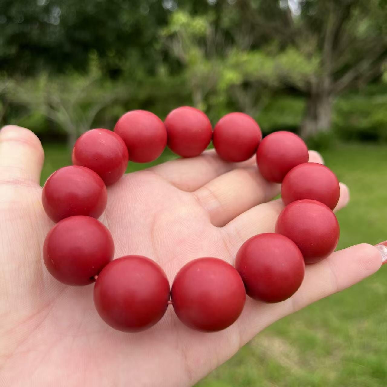 Red beaded bracelet on a hand with a blurred green outdoor background