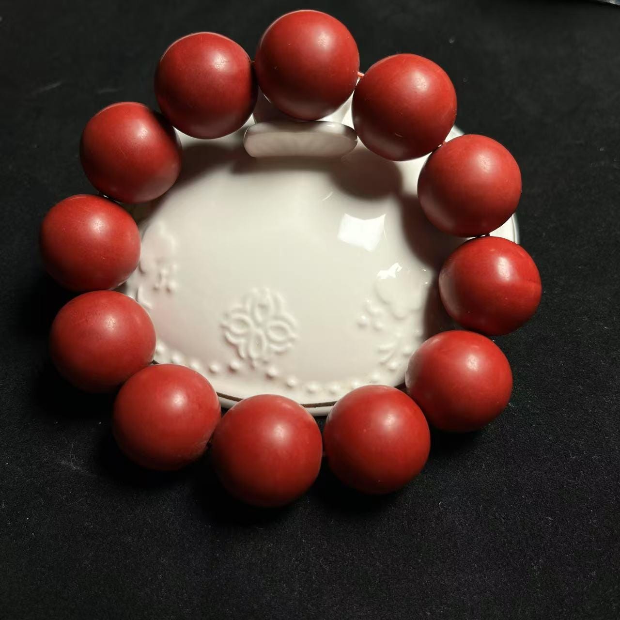 Red beaded bracelet on a white dish against a black background