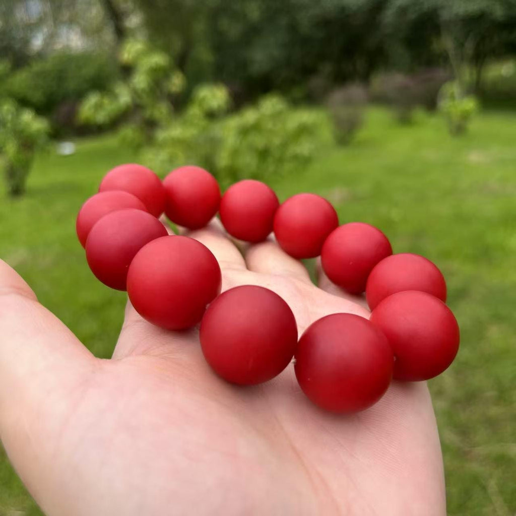 Red beaded bracelet held in a hand with a blurred green outdoor background