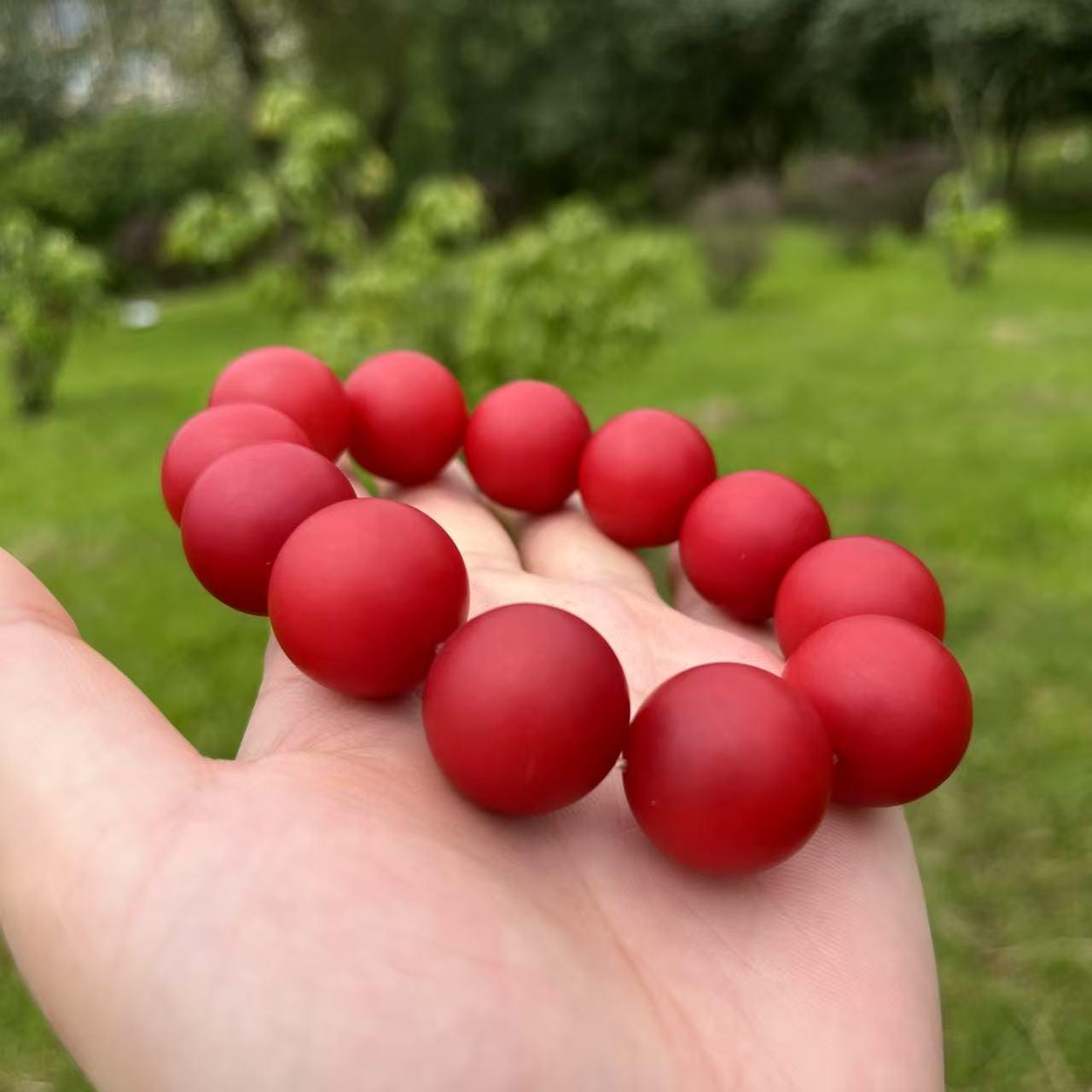 Red beaded bracelet held in a hand with a blurred green outdoor background