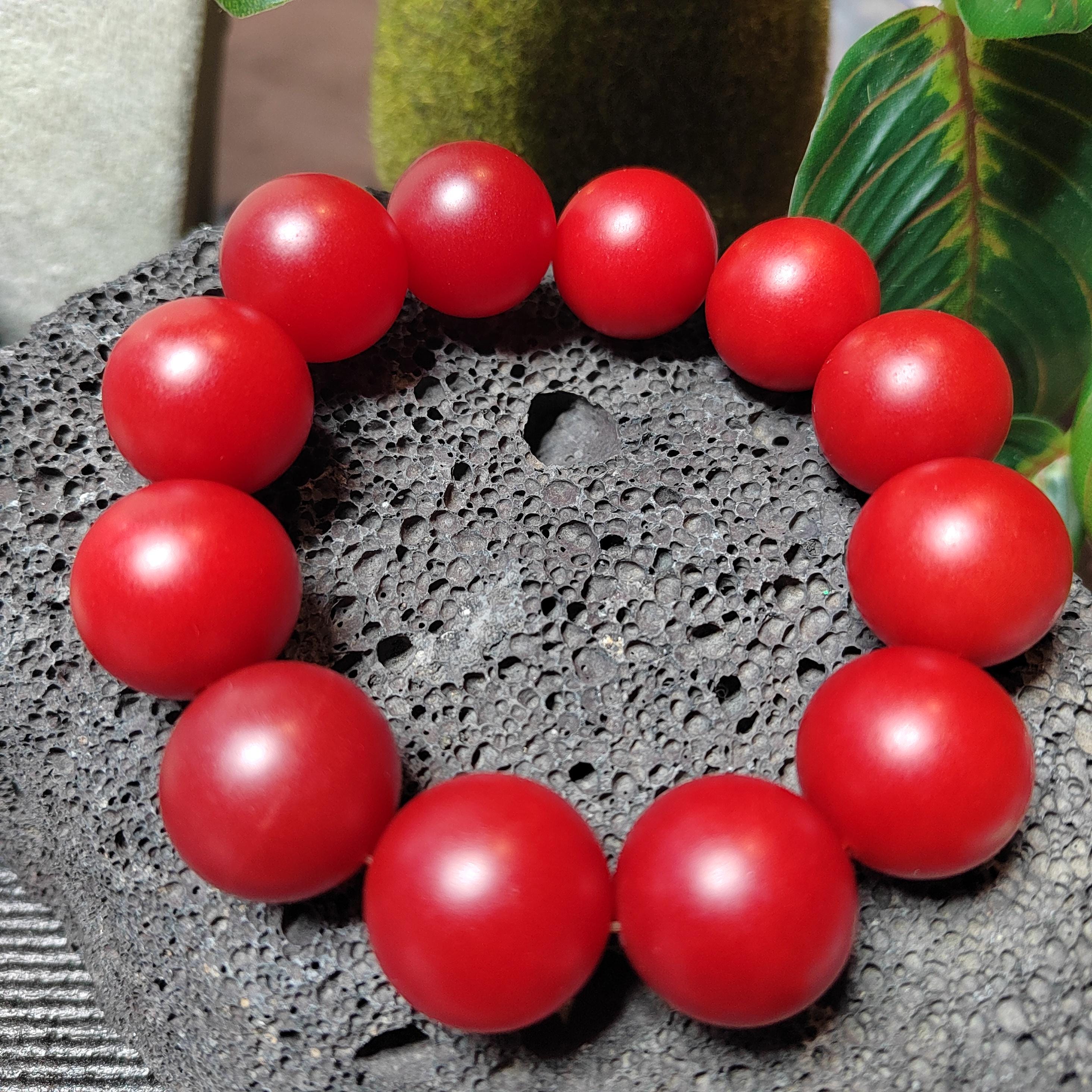 Red beaded bracelet on a textured surface with green leaves in the background