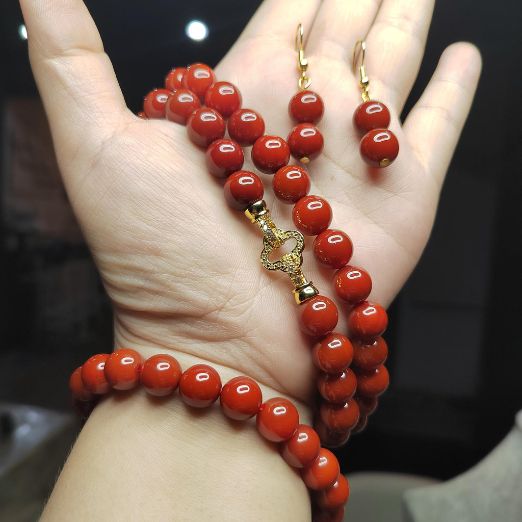Red beaded bracelet and earrings on a hand with a dark background