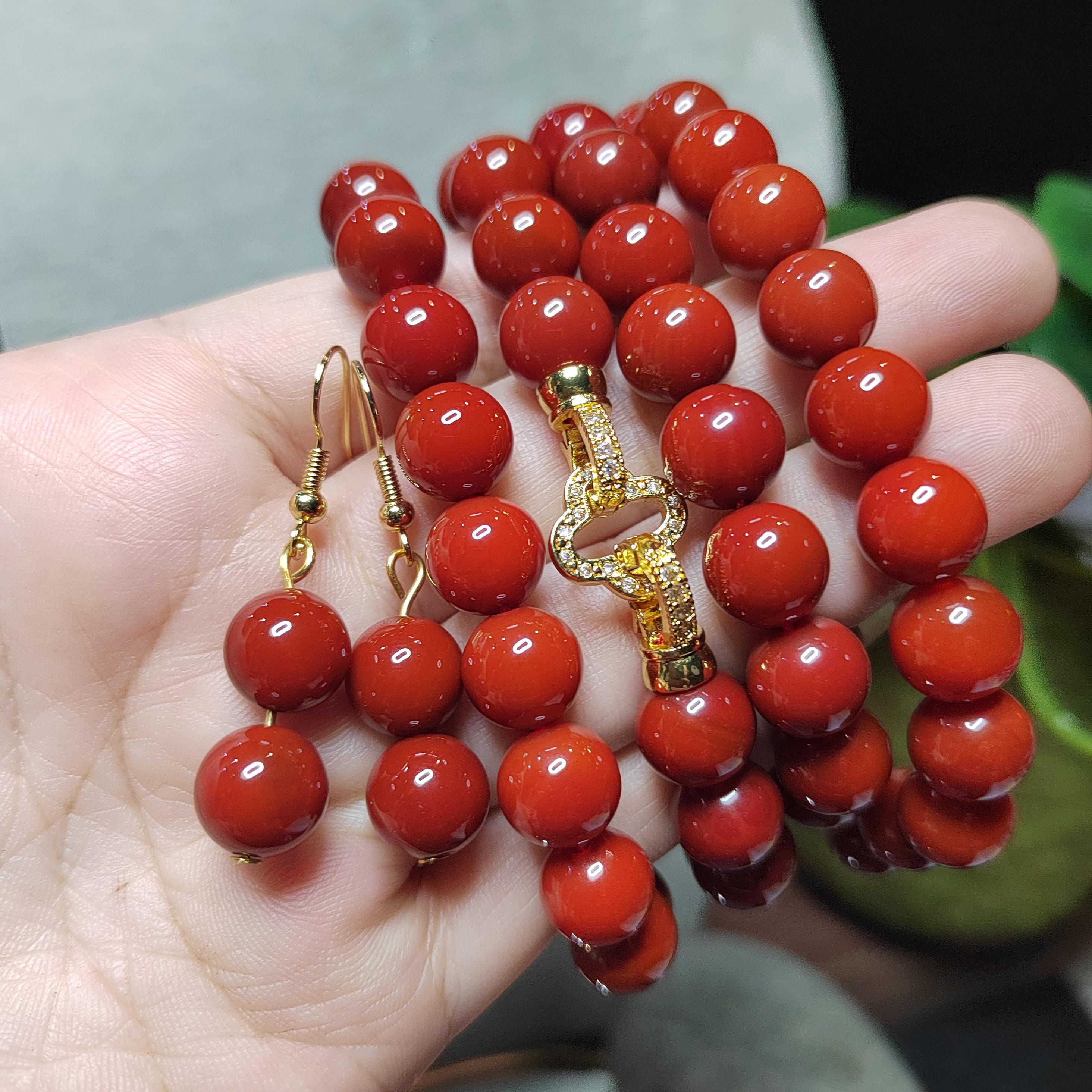 Red beaded necklace and earrings on a hand with a blurred background