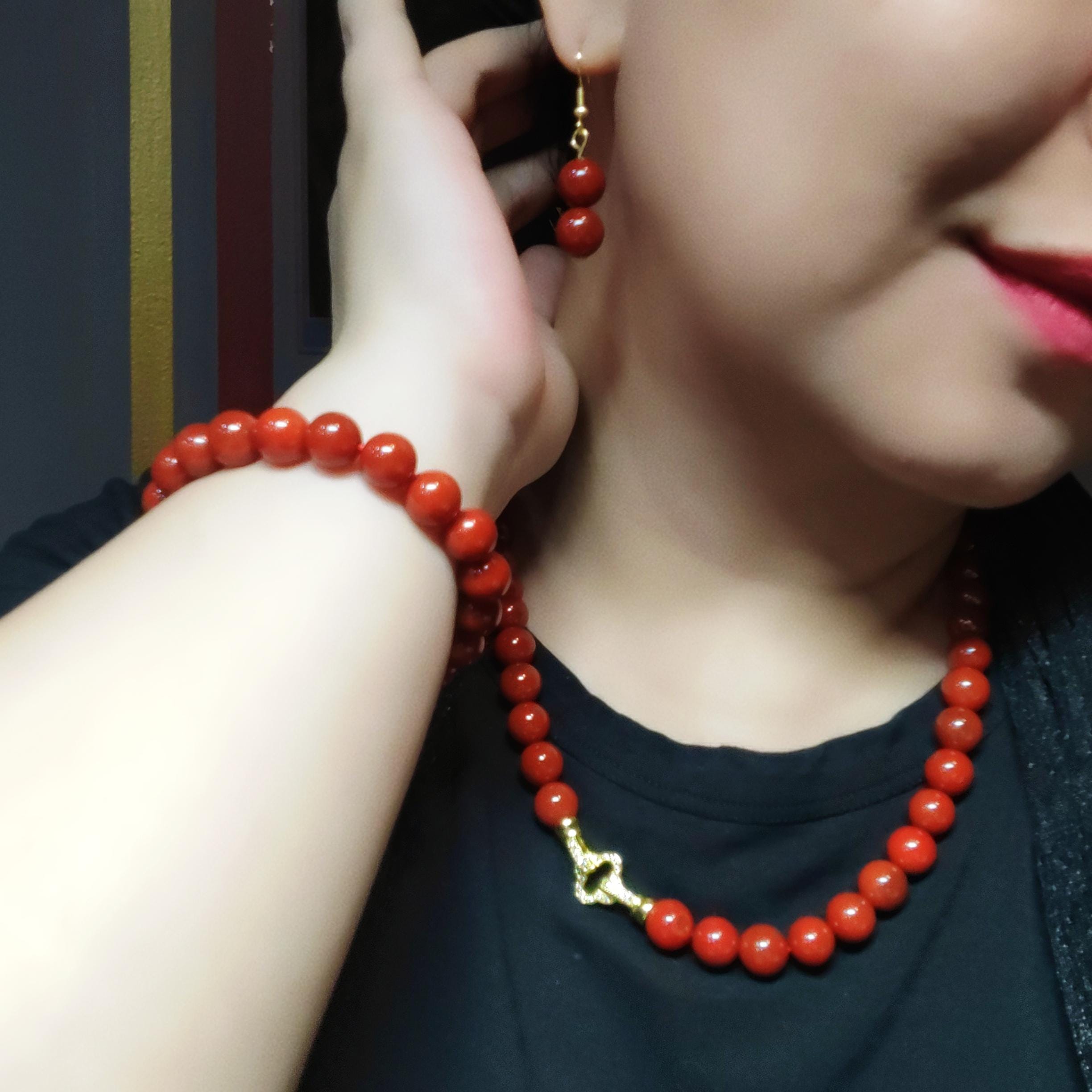 Person wearing a red beaded necklace with a gold clasp against a dark background