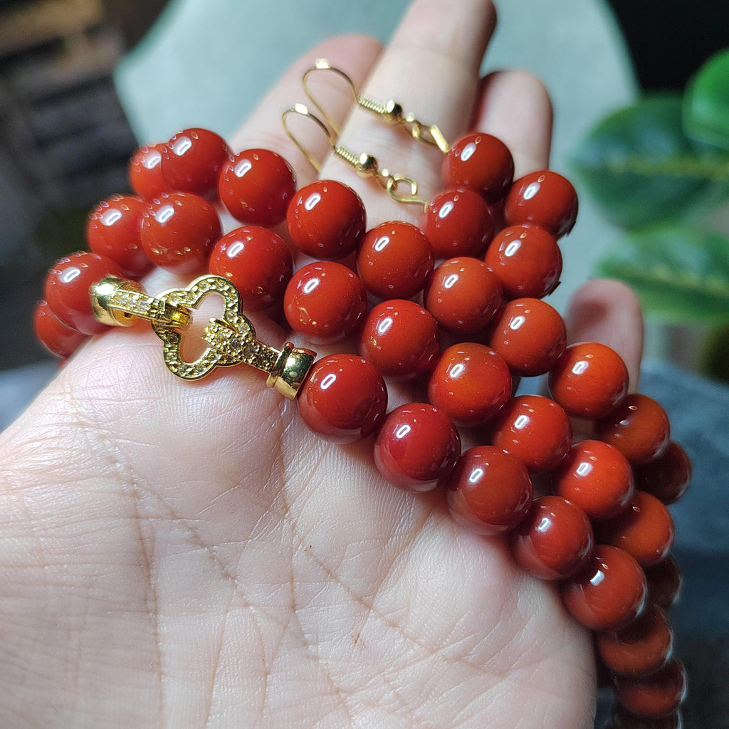 Red beaded bracelet with a gold clasp held in a hand against a blurred background