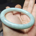 Light blue-green jade bracelet held in a hand against a neutral background