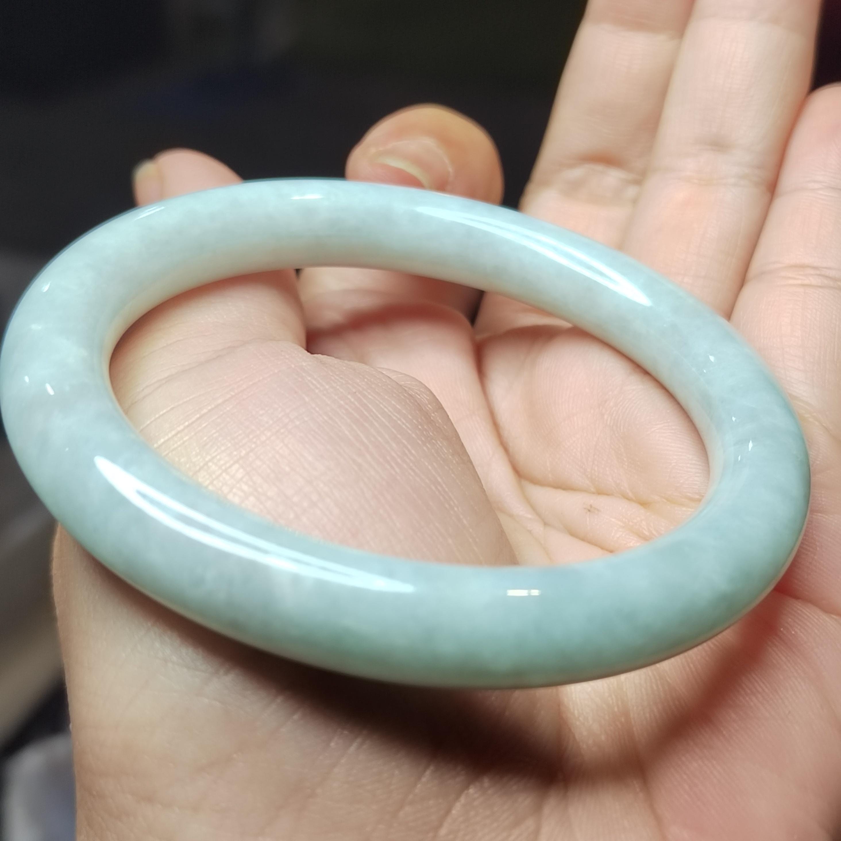 Light blue-green jade bracelet held in a hand against a neutral background