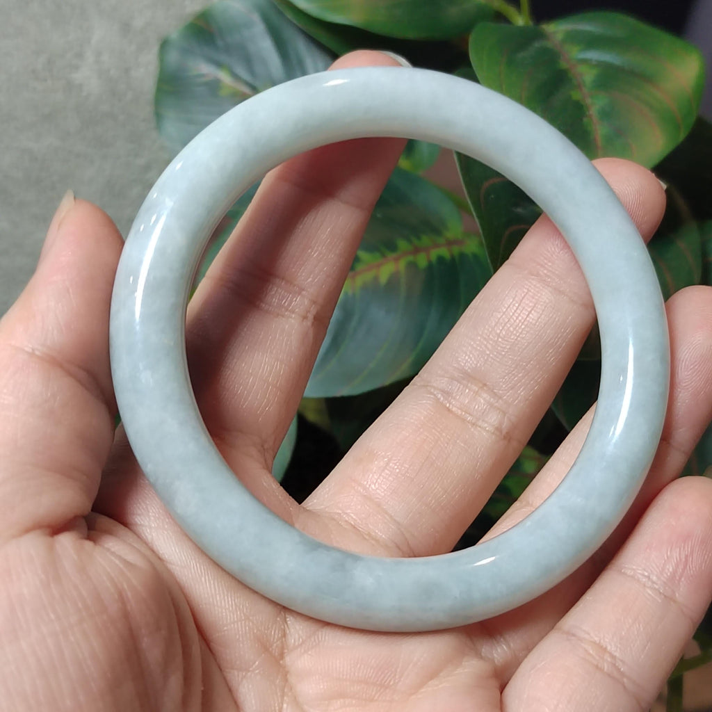 Light blue jade bracelet held in a hand with a green leafy background