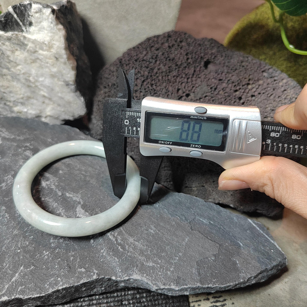 Digital caliper measuring a jade ring on a stone surface