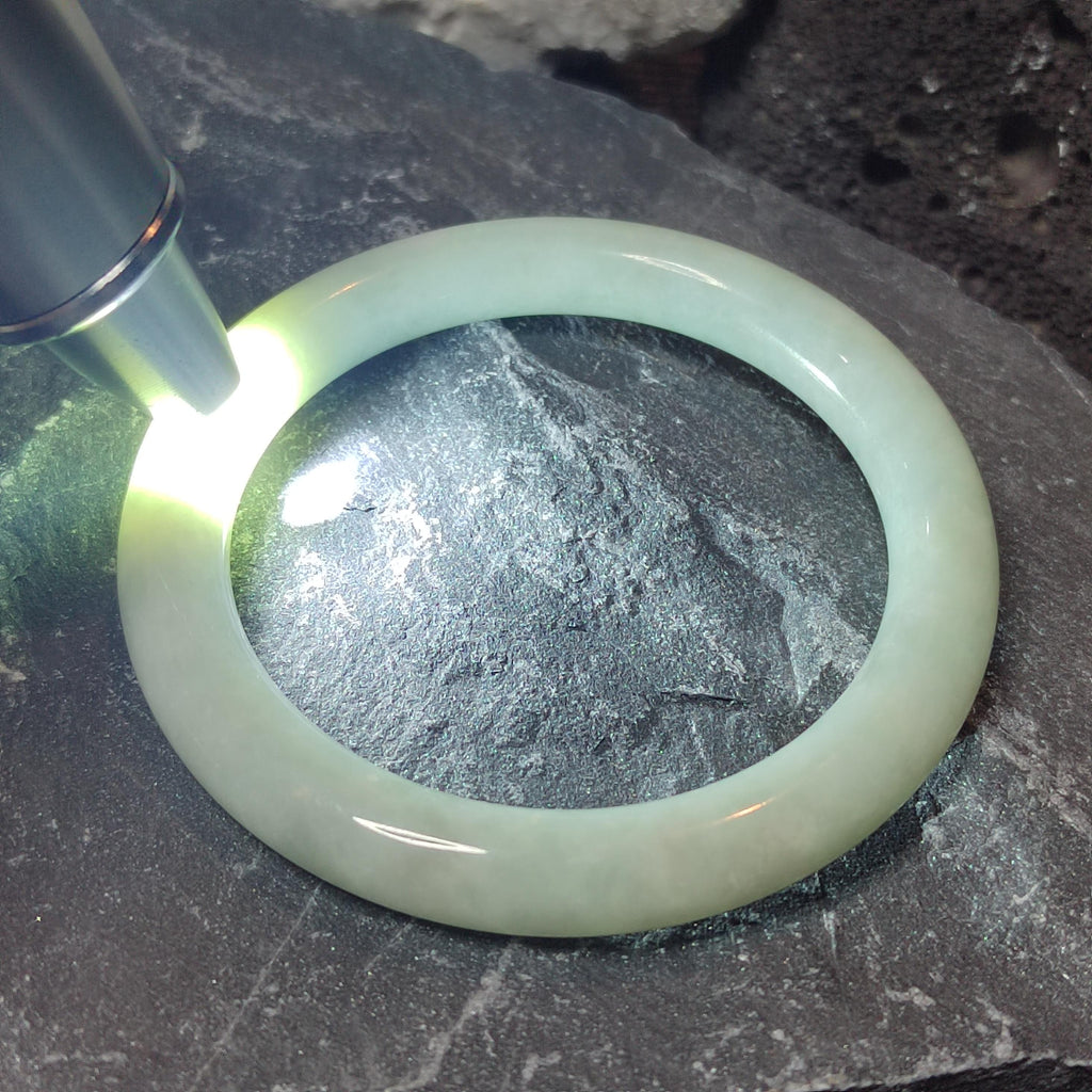 Green jade bracelet under a magnifying glass on a dark stone surface