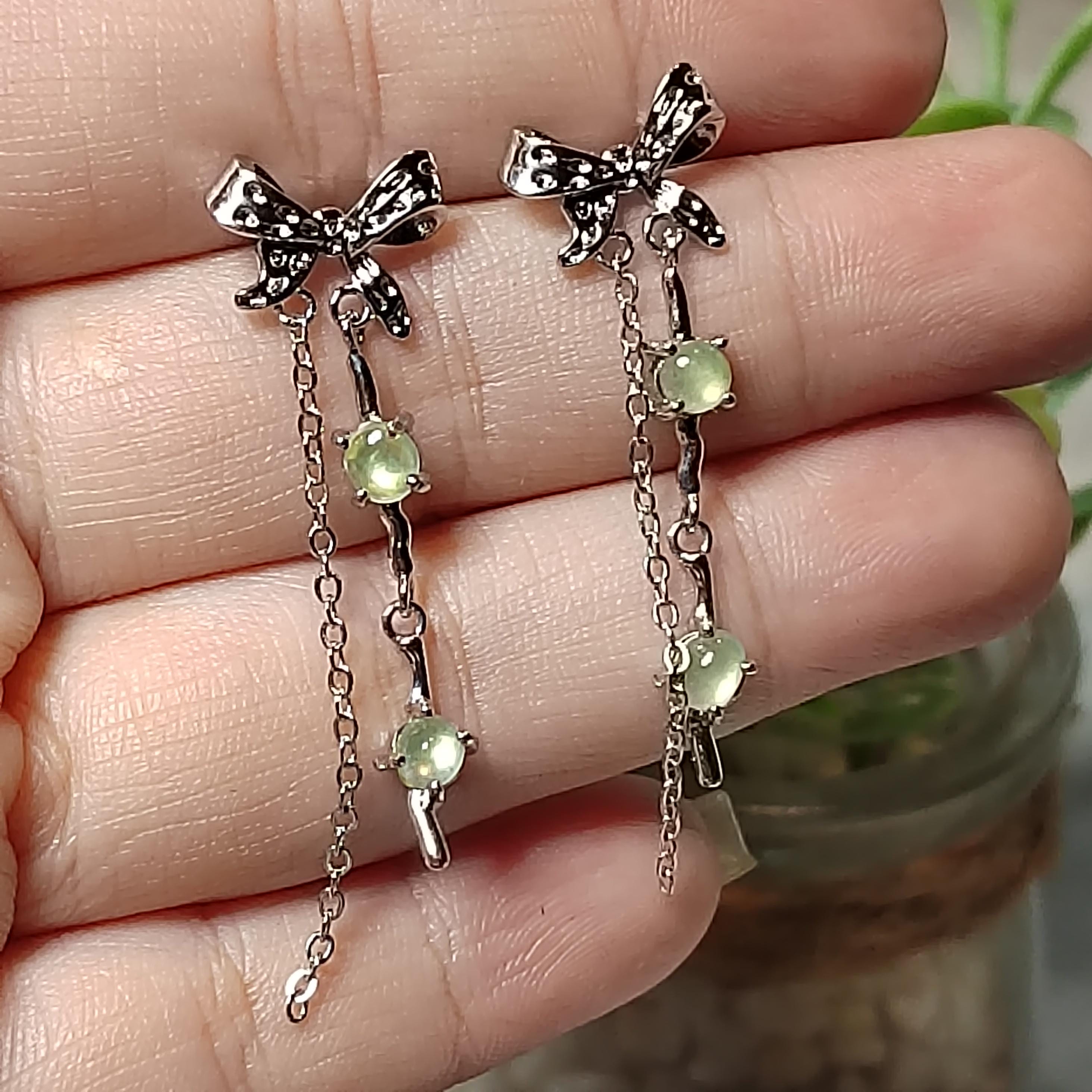 Silver bow earrings with green gemstones held between fingers