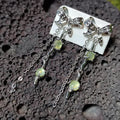 Silver earrings with bow designs and green gemstones on a textured surface