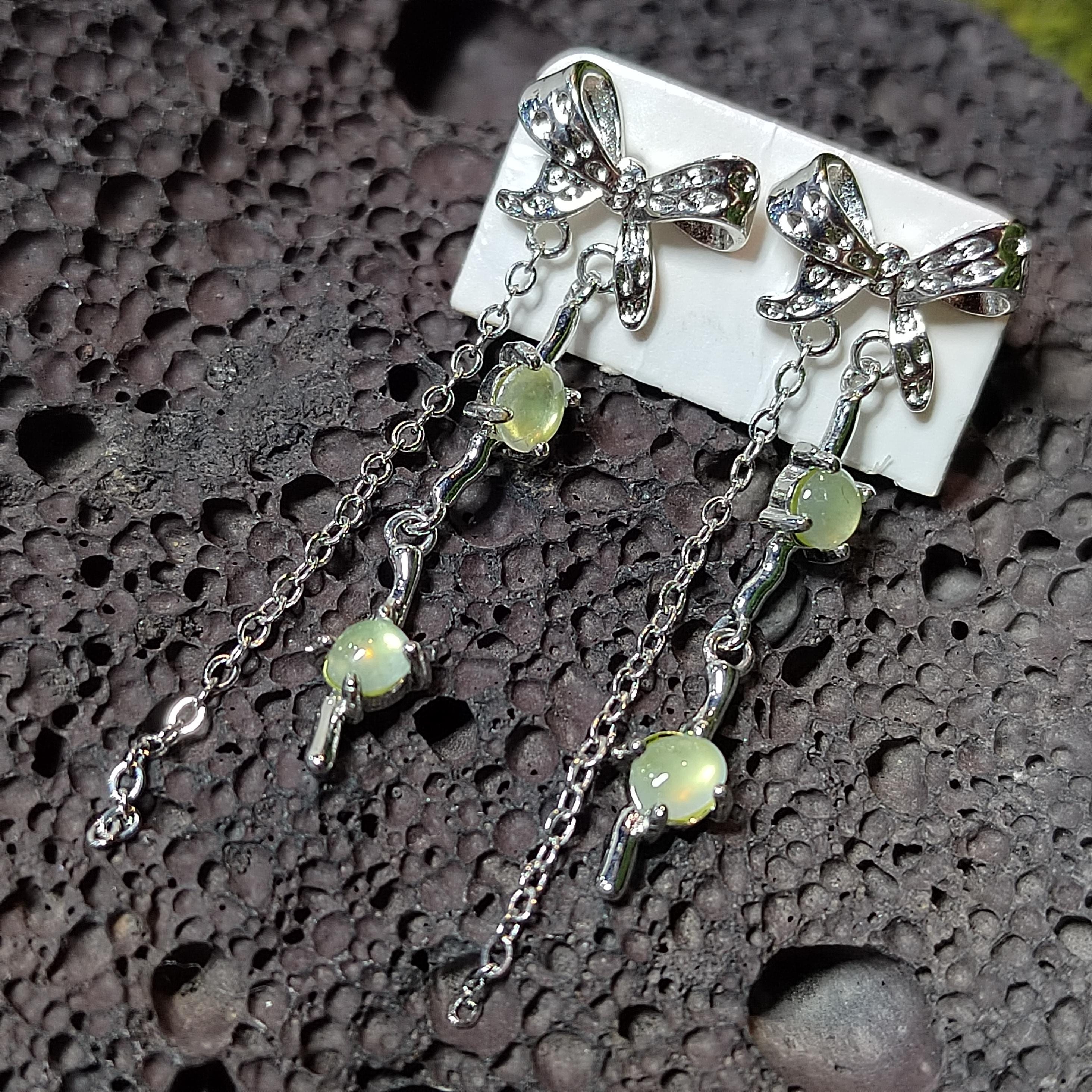 Silver earrings with bow designs and green gemstones on a textured surface