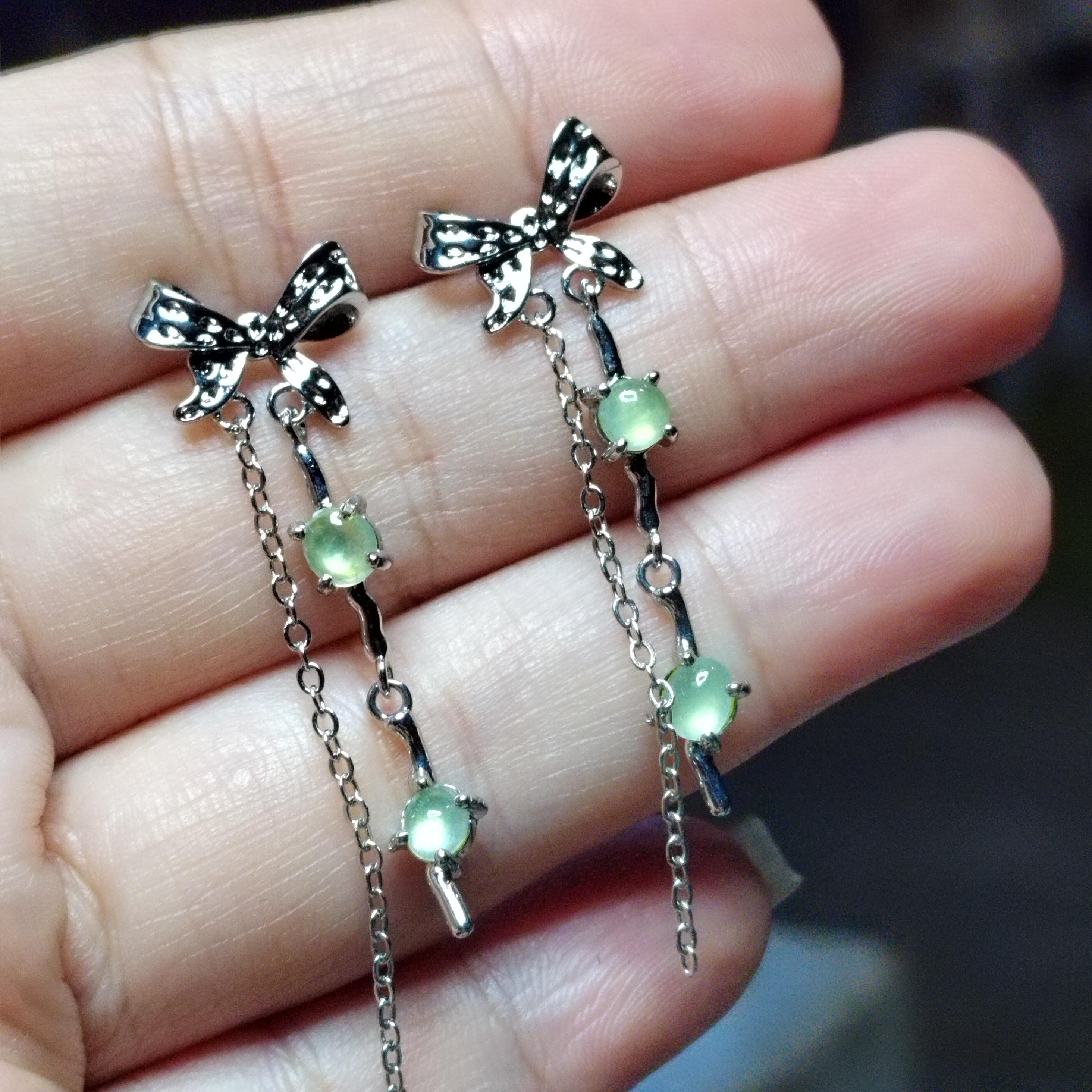 Silver bow earrings with green gemstones held between fingers