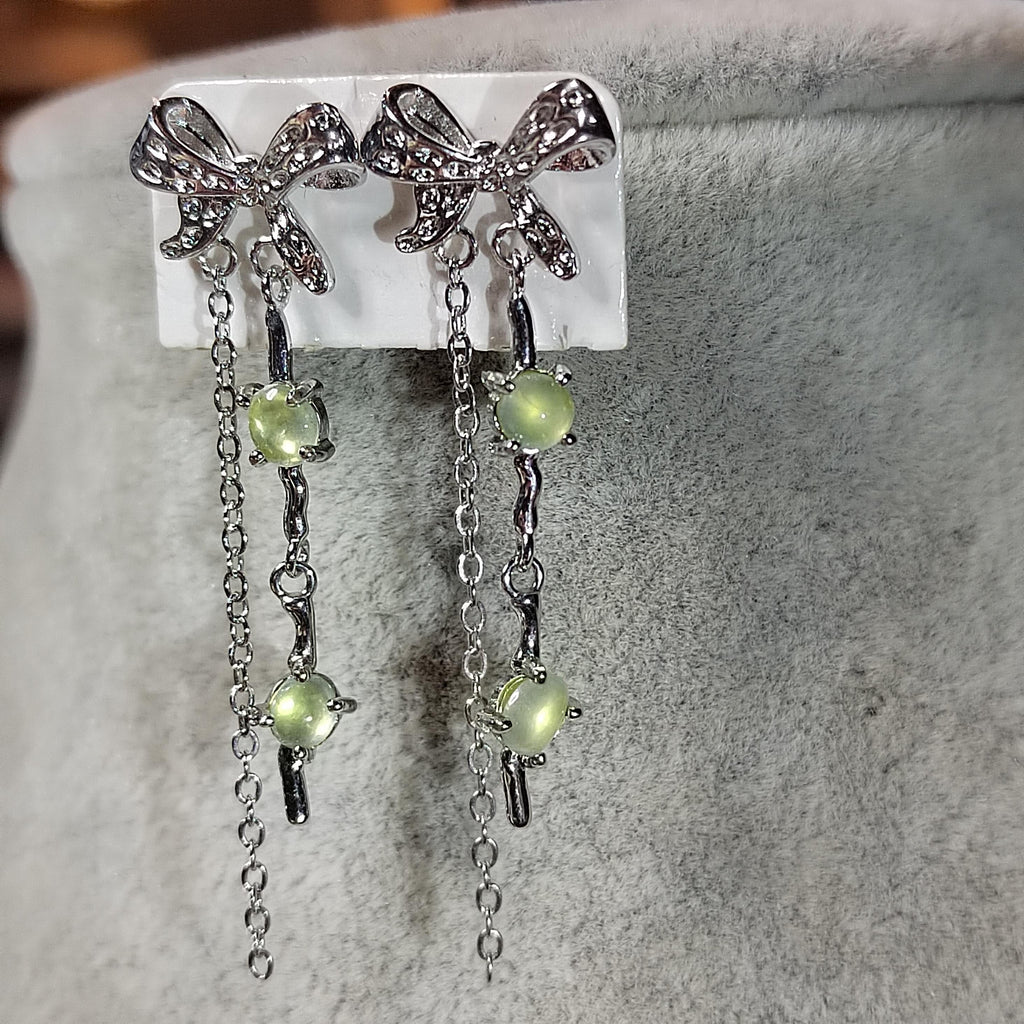 Butterfly-shaped earrings with green gemstones on a gray surface