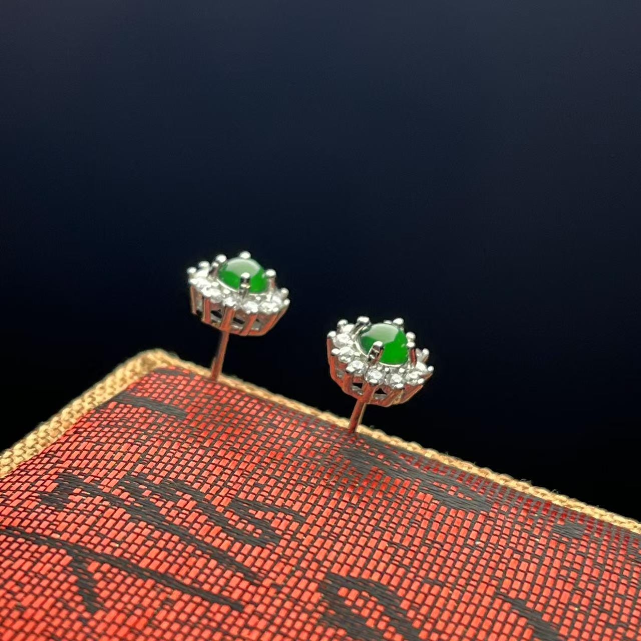 Pair of earrings with green gemstones on a textured red surface