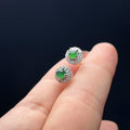 Jadeite earrings held between fingers against a dark background