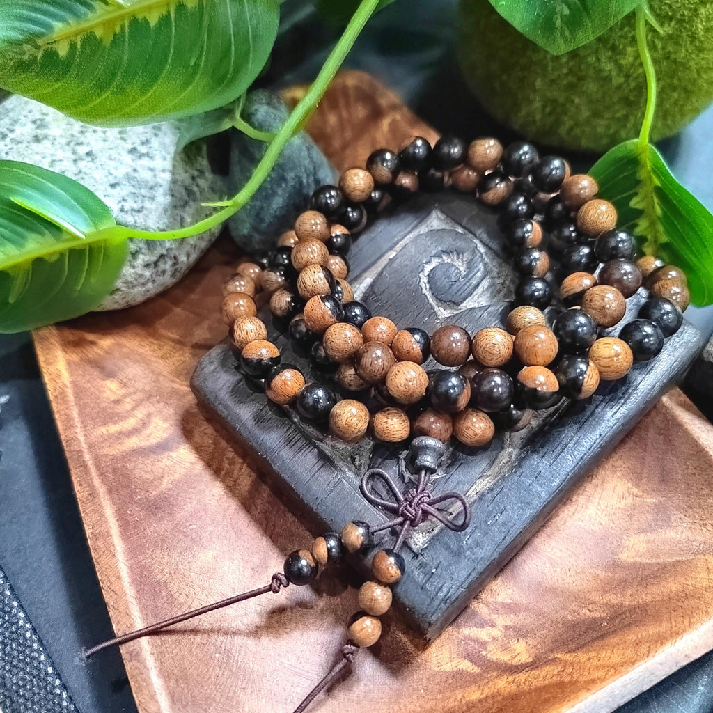 Wooden beaded bracelet on a dark stone surface with green leaves in the background