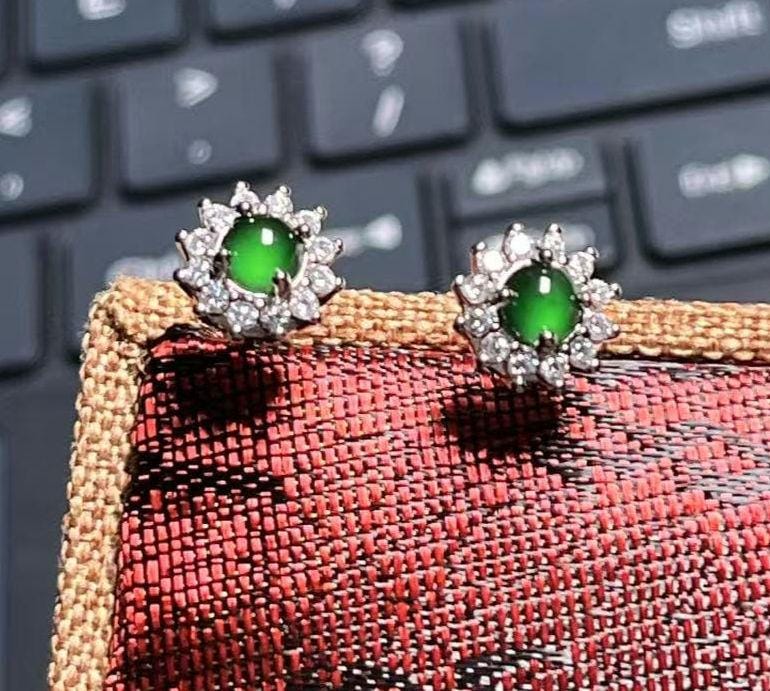 Green gemstone earrings on a textured surface with a keyboard in the background