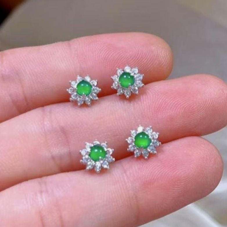 Green gemstone earrings held between fingers against a neutral background