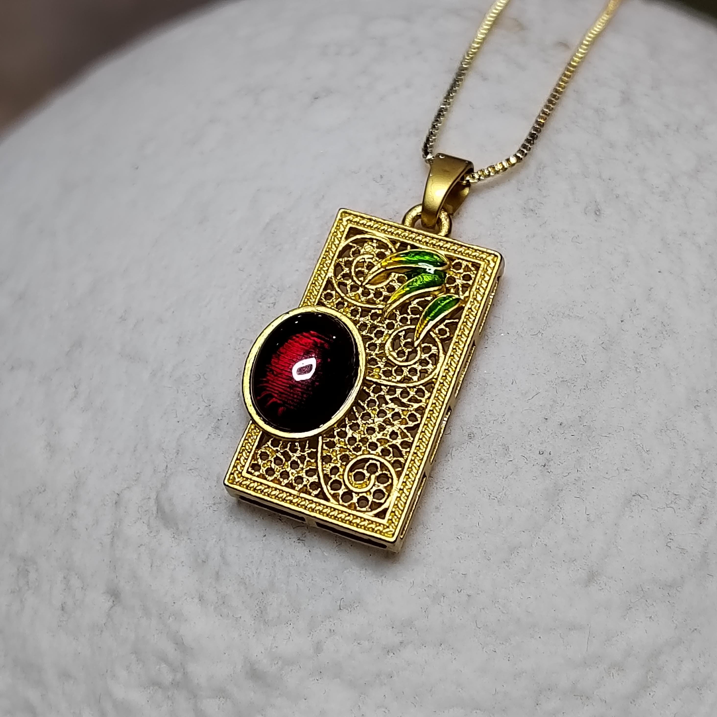 Gold pendant with intricate design and red amber on a gray surface