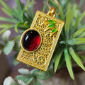 Gold pendant with red and black stone on green leaves