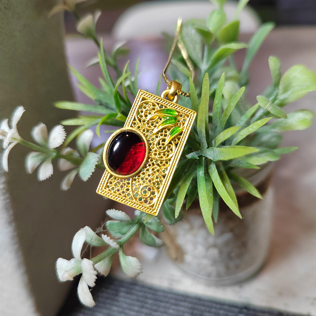 Gold pendant with a red amber on a plant background