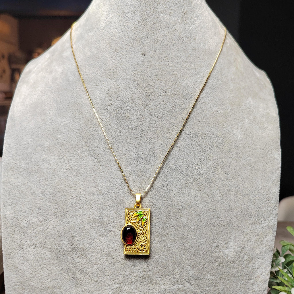 Gold necklace with a rectangular pendant featuring a red amber on a gray stand.