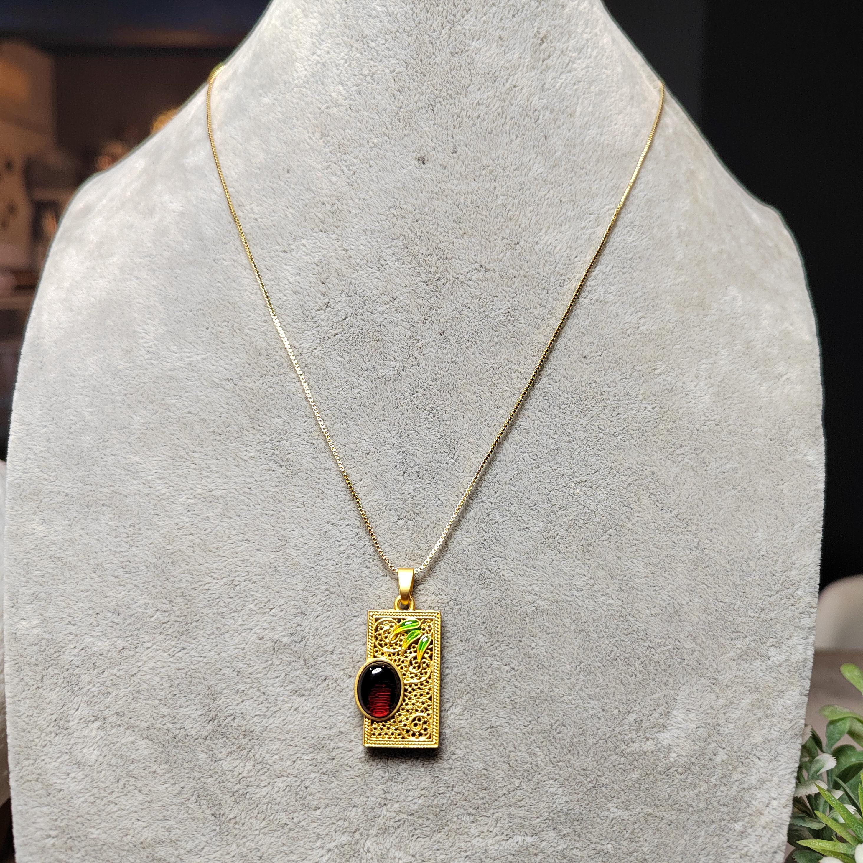 Gold necklace with a rectangular pendant featuring a red amber on a gray stand.