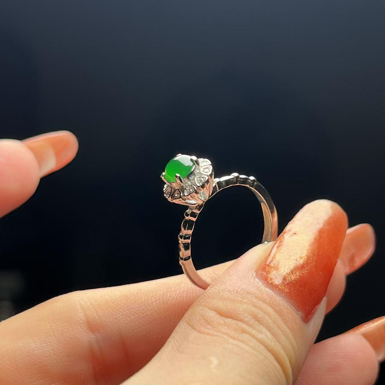 Silver ring with a green gemstone held on a finger against a dark background