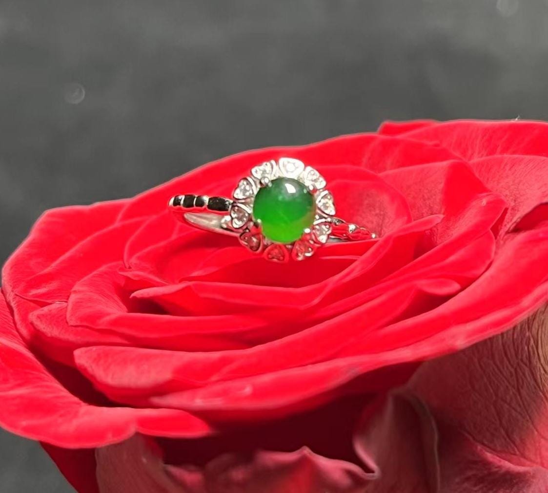 Green gemstone ring on a red rose with a dark background