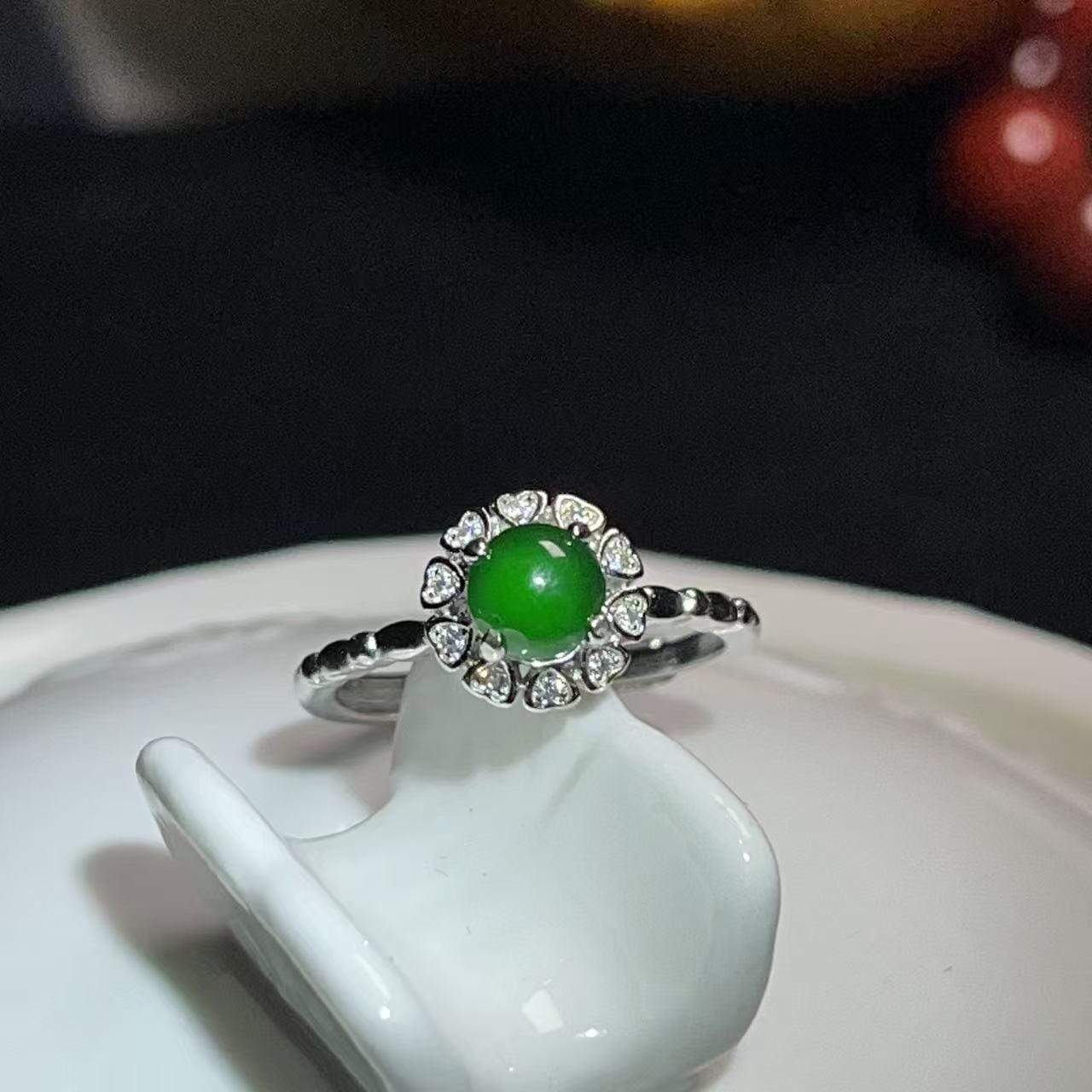 Green gemstone ring with silver setting on a white stand against a dark background
