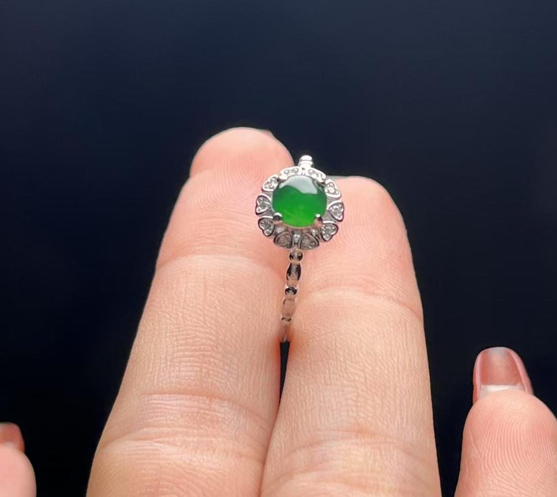 Silver ring with a green gemstone on a finger against a dark background