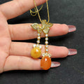 Butterfly-shaped necklace with orange beads held by a hand on a black background