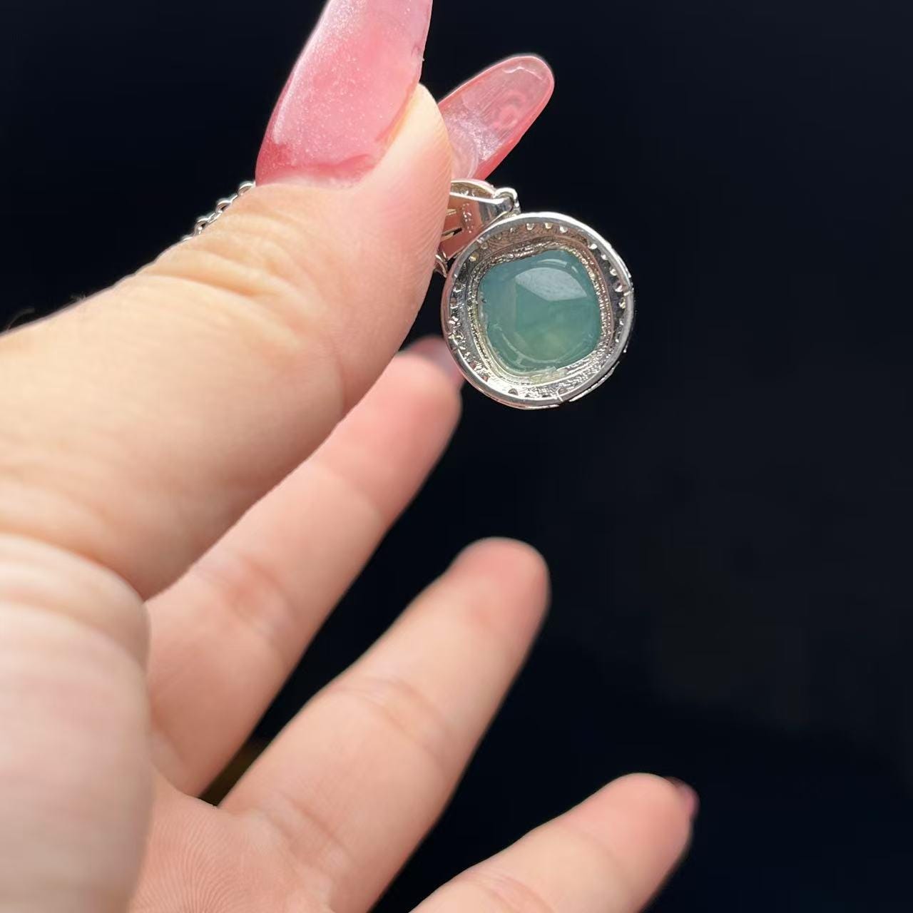 Silver pendant with a green gemstone held by a hand against a dark background