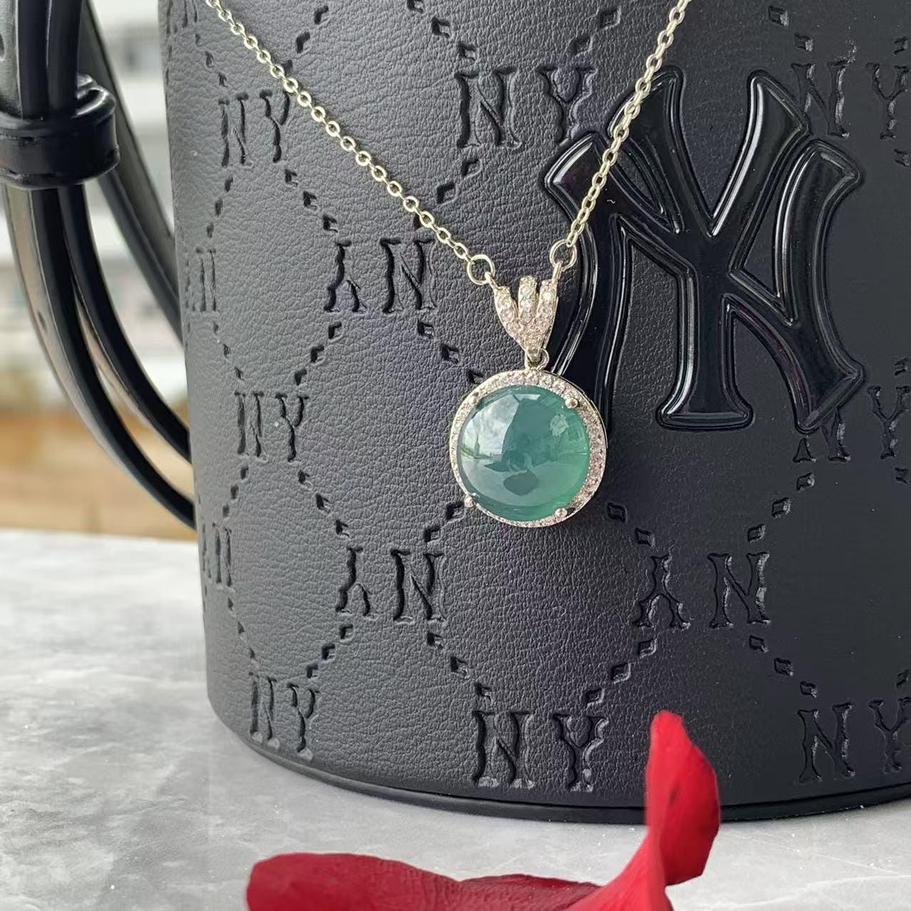 Necklace with a green pendant on a black handbag with 'NY' branding.
