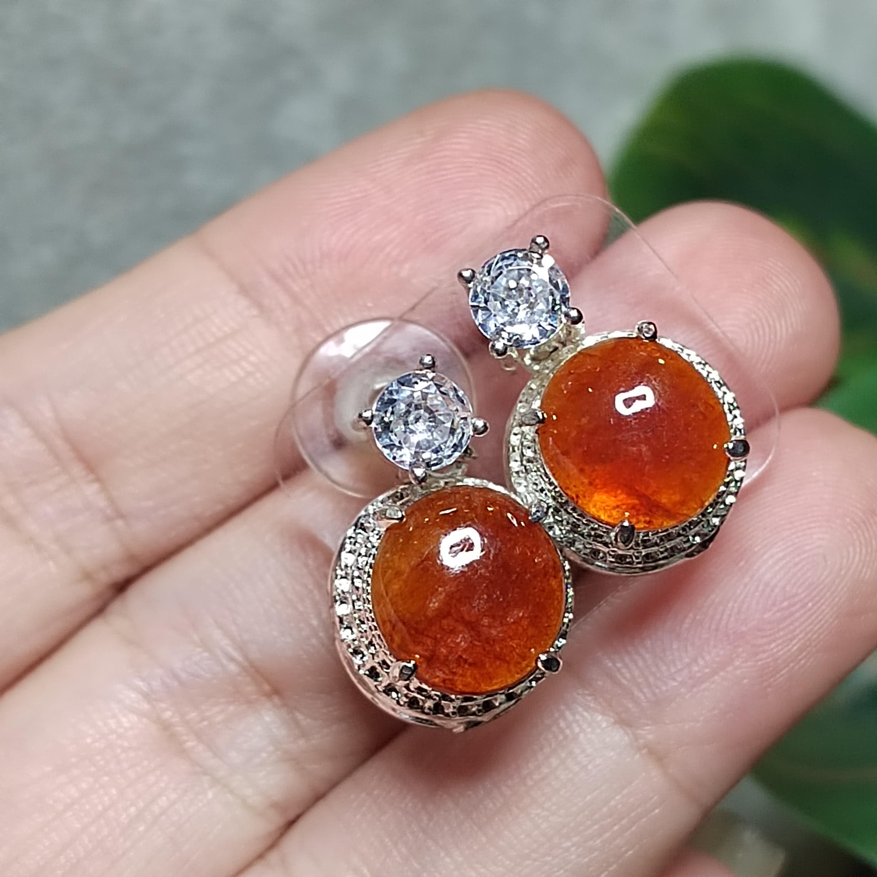 Pair of earrings with orange gemstones and clear stones held between fingers.